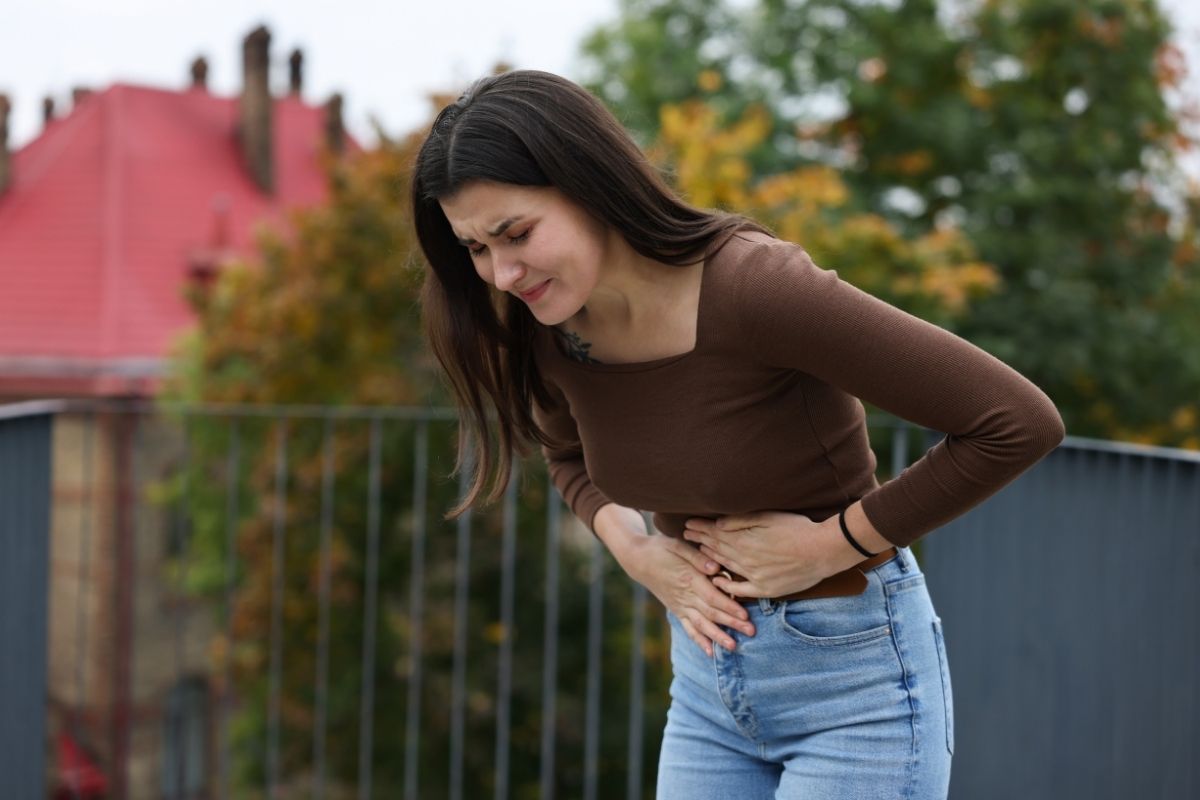 Hasi fájdalmat tapasztaló nő, a stressz és emésztési panaszok kapcsolatának szemléltetésére.